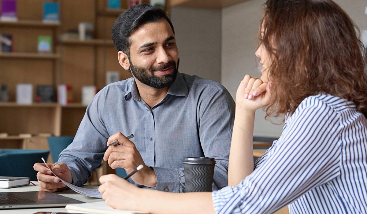 interview of happy smiling indian hr manager with latin young professional and friendly support discussing job cv. mentoring hispanic male teacher and female student in multiethnic creative space.